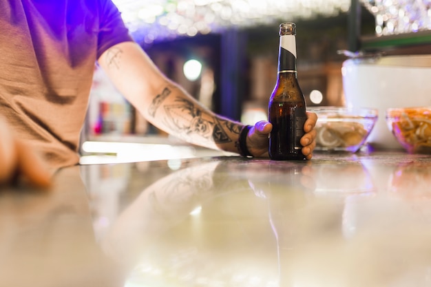 Tattoo man holding alcohol bottle on reflective table