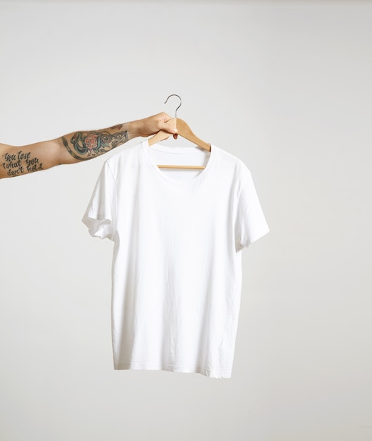 Free Photo tattooed biker hand holds hang with blank white t-shirt from premium thin cotton, isolated on white