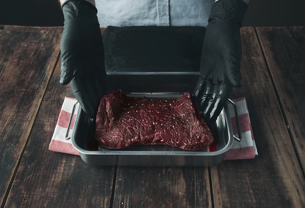 Free photo tattooed butcher hands in black gloves offer piece of fresh raw meat in stainer with juice or blood on camera