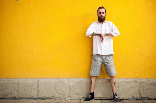 Free photo tattooed fashion bearded hipster on yellow wall posing outdoor