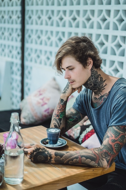 Free photo a tattooed man drinks a colorful coffee in a cafe.