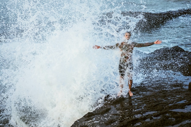 Free photo a tattooed man lies on the edge of a cliff. splashes of ocean waves.