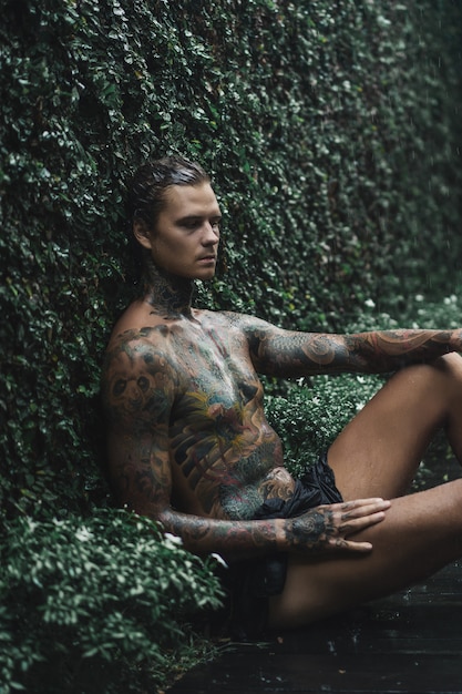 Free photo tattooed man posing in the rain