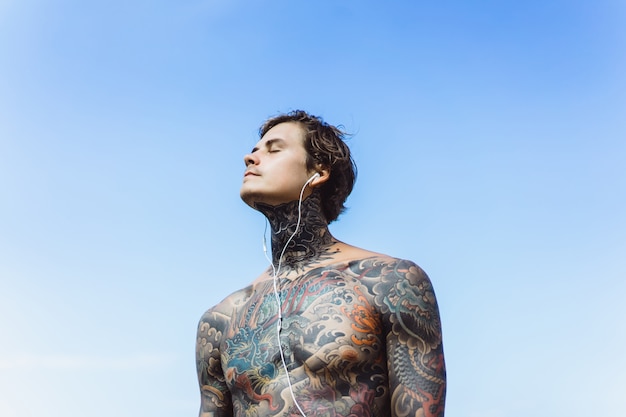 Free photo tattooed man with headphones against the blue sky on the ocean