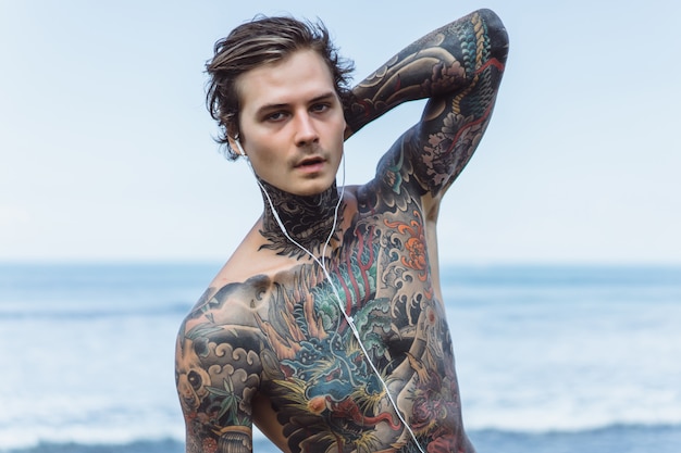 Free Photo tattooed man with headphones against the blue sky on the ocean