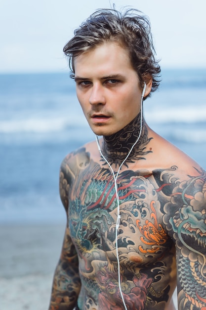 Free Photo tattooed man with headphones against the blue sky on the ocean.