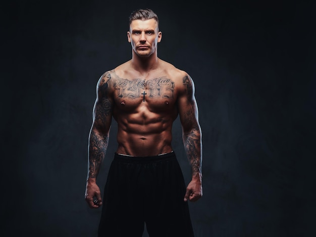 Free Photo a tattooed muscular shirtless man with stylish hair posing at the camera on a dark background.