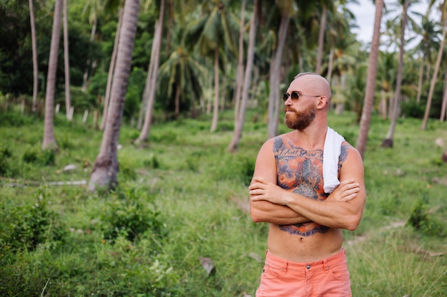 Tattooed strong man on jungle tropical field without shirt