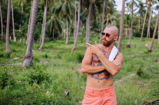 Free photo tattooed strong man on jungle tropical field without shirt