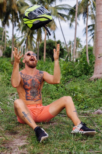 Free Photo tattooed strong man on tropical jungle field with red motorbike