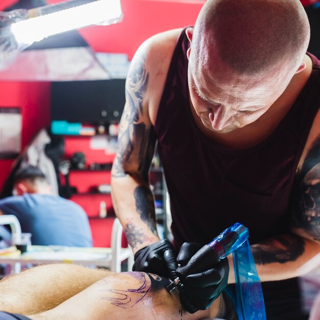 Tattooer drawing with machine on leg in studio