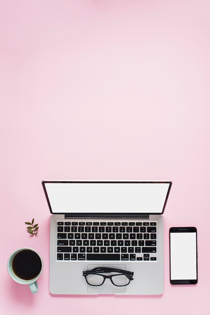 Tea cup; eyeglasses; mobile phone and an open laptop with white screen against pink background