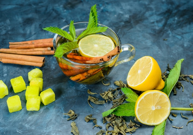 Free photo tea in a cup with lemon, mint, cinnamon sticks, sugar cubes high angle view on a blue surface