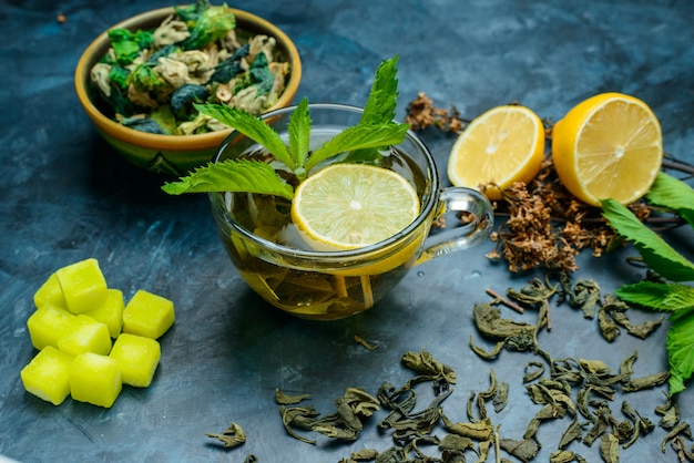 Free photo tea in a cup with mint, dried herbs, lemon, sugar cubes high angle view on a blue surface