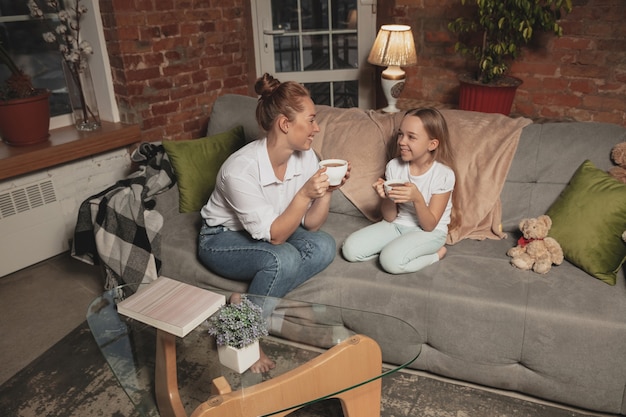 Tea drinking, talking. Mother and daughter during self-insulation at home while quarantined, family time cozy, comfort, domestic life. Cheerful, happy smiling models. Safety, prevention, love concept.