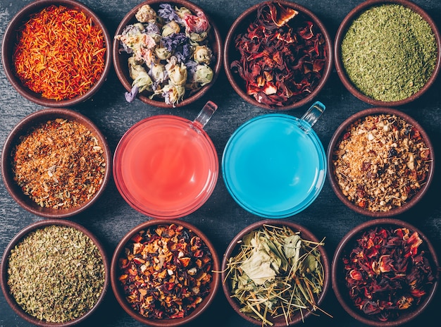 Free photo tea herbs in a bowls with red and blue colored water top view on a dark textured background