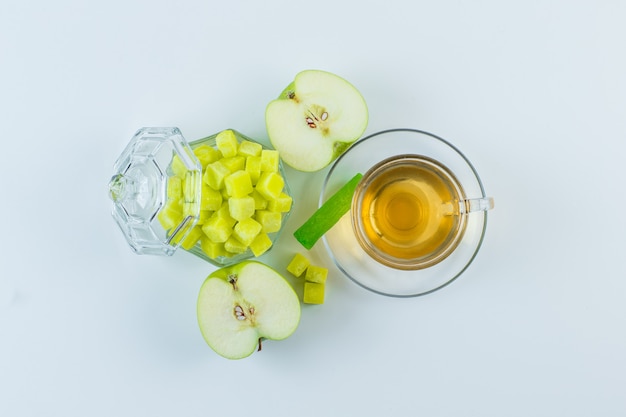 Tea in a mug with apple, sugar cubes, candy flat lay on a white background