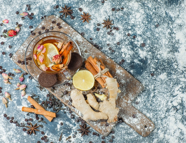 Tea in a mug with flour, choco, biscuits, spices, lemon, herbs top view on concrete and cutting board