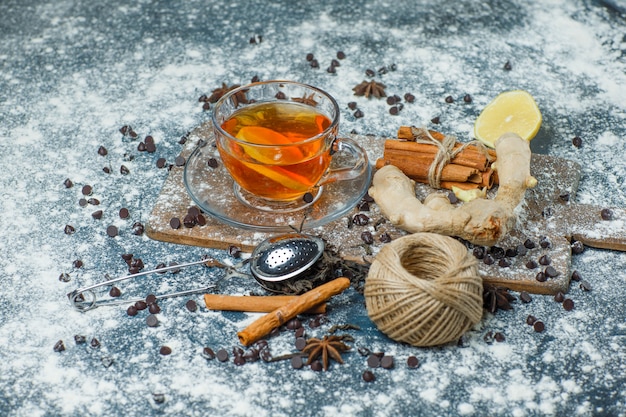 Free photo tea in a mug with flour, choco chips, strainer, spices, lemon high angle view on concrete and cutting board