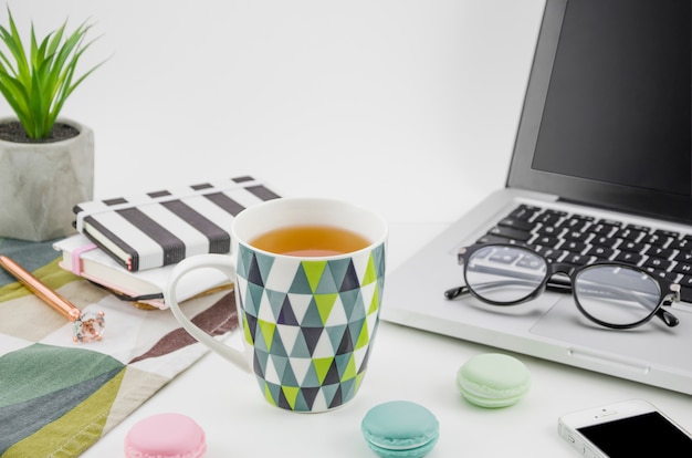 Free Photo tea mug with macaroons on white working desk with laptop and mobile phone