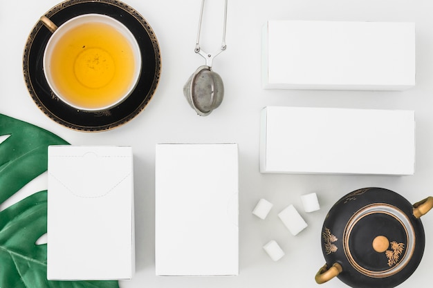 Tea strainer and white boxes with sugar cubes on white background