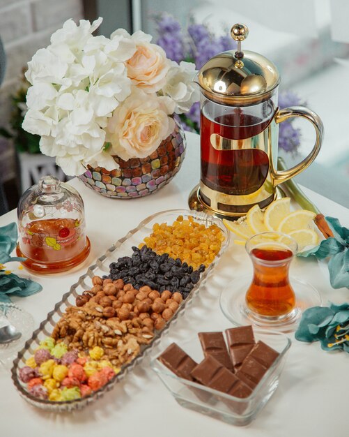 Tea table with kettle, glass of tea, nuts and sweets.