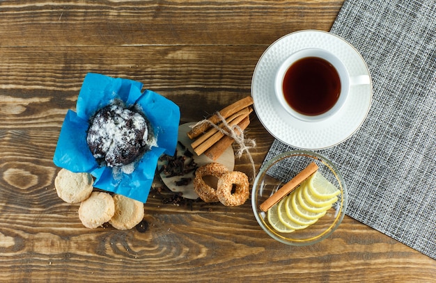 Tea with biscuits, cloves, lemon slices, cinnamon sticks in a cup on wooden surface