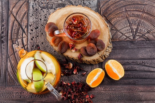 Tea with dried fruits, herbs, fruit infused water, orange, wood in a cup on stone tile surface, top view