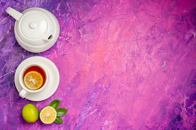 Free Photo tea with lemon a cup of tea with lemon next to the teapot and limes on the left side of the pink-purple table