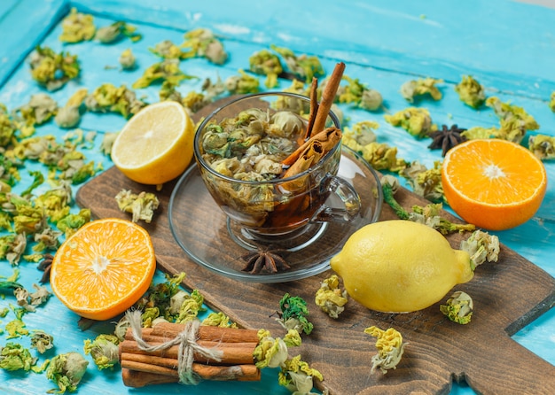 Free photo tea with spices, orange, lemon, dried herbs in a mug on blue and cutting board, high angle view.