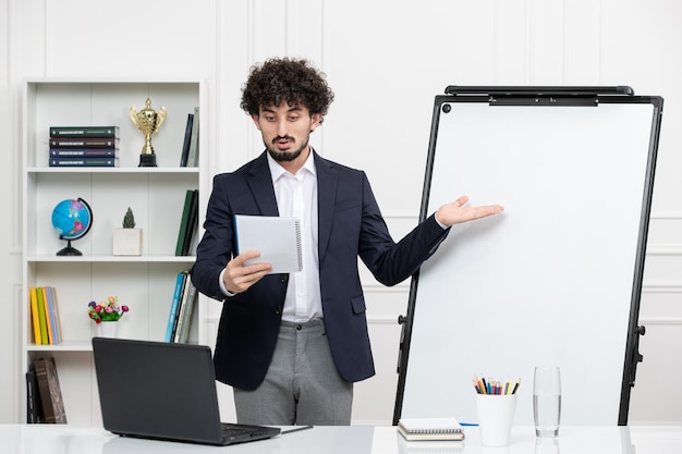 Teacher brunette instructor with computer in suit and whiteboard in classroom reading notes