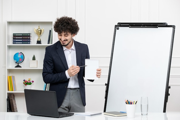 Teacher brunette instructor with computer in suit and whiteboard in classroom smiling holding notes