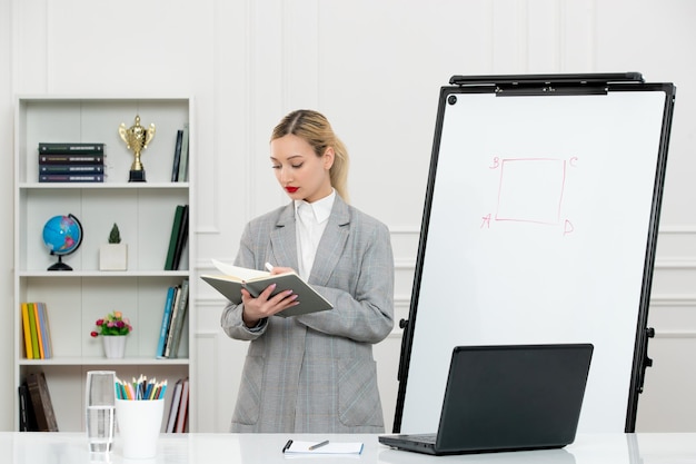 Teacher cute instructor in suit in classrom with computer and whiteboard reading a book