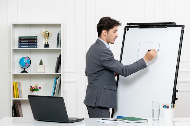 Teacher smart instructor in grey suit in classroom with computer and whiteboard drawing square