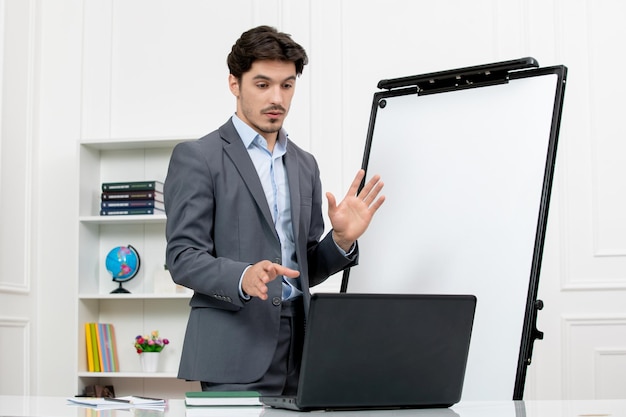 Teacher smart instructor in grey suit in classroom with computer and whiteboard explaining lecture