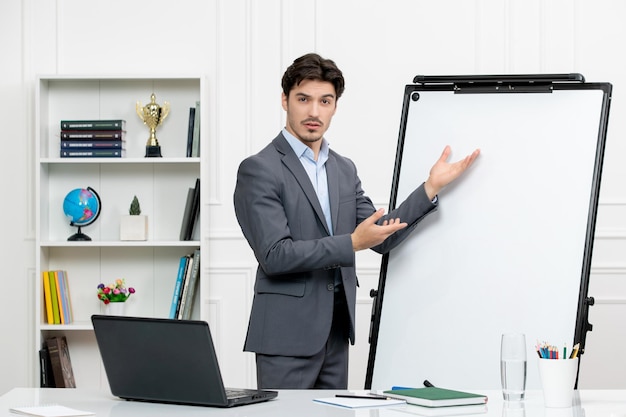 Teacher smart instructor in grey suit in classroom with computer and whiteboard explaining math