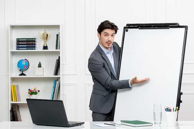 Free photo teacher smart instructor in grey suit in classroom with computer and whiteboard presenting board