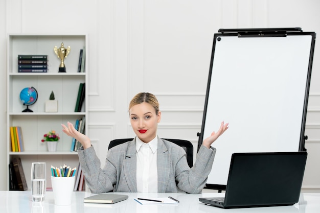 Teacher young cute instructor in grey suit in classrom with laptop and whiteboard waving hands