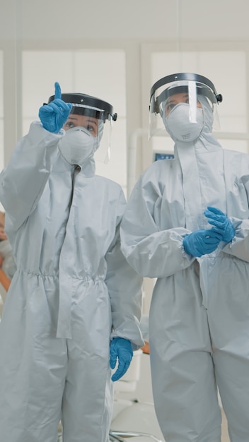 Team of caucasian dentists with hazmat suits discussing prevention