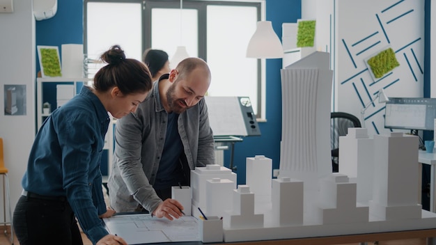 Team of colleagues using building model for inspiration to design construction layout. Man and woman working with maquette to plan blueprints and urban structure. Architectural project