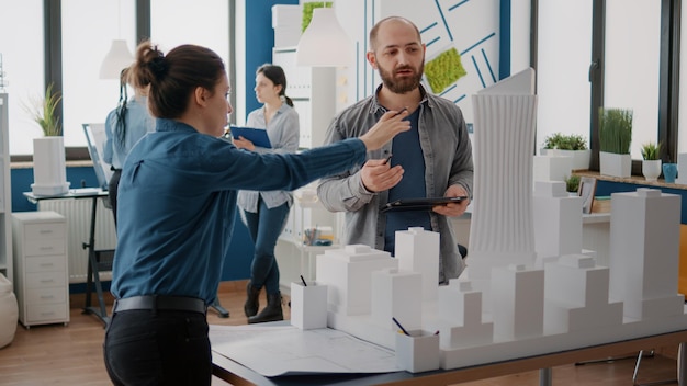 Free photo team of coworkers analyzing maquette and building model to plan construction on tablet. architectural people working together, designing urban strategy and real estate development.