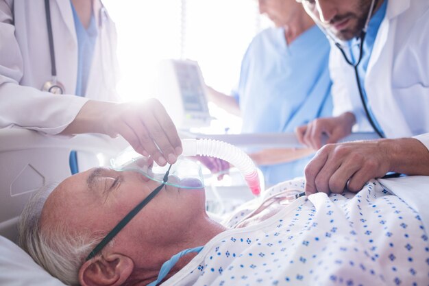 Team of doctors putting oxygen mask on a male senior patient face