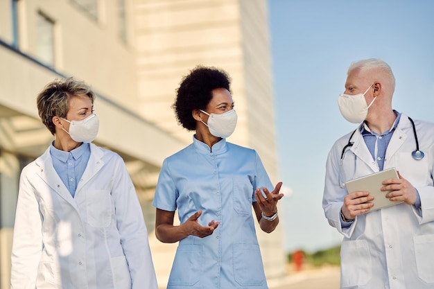 Free photo team of happy doctors communicating while walking outdoors with protective masks on their faces