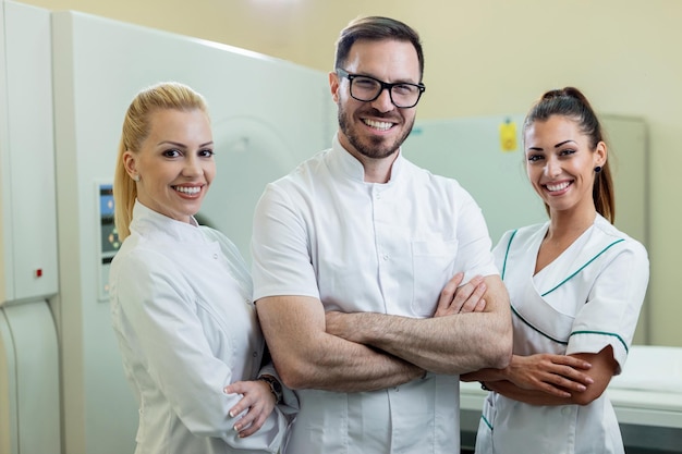 Free photo team of happy doctors standing with arms crossed next to mri scanner in the hospital and looking at camera