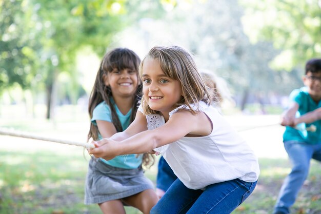 Team of happy kids pulling rope, playing tug-of-war, enjoying outdoor activities. Group of children having fun in park. Childhood or teamwork concept