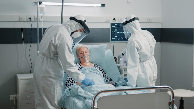 Team of paramedics in hazmat suits checking on patient healthcare. Medical staff with protection against coronavirus outbreak consulting woman with oxygen tube in quarantine isolation zone