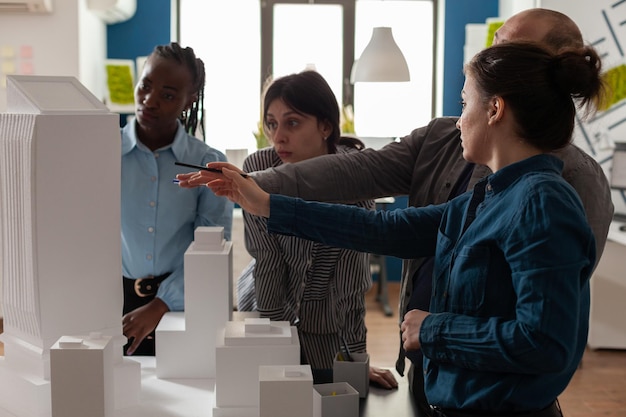 Team of professional architects brainstorming ideeas pointing at real estate construction model in architectural office. Mixed group of engineers working on residential project at desk.