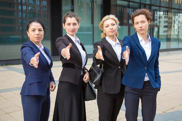 Free Photo team of serious confident businesswomen standing together near office building, offering handshake, looking at camera. front view. cooperation concept