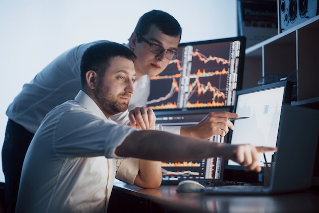 Team of stockbrokers are having a conversation in a dark office with display screens. Analyzing data, graphs and reports for investment purposes. Creative teamwork traders