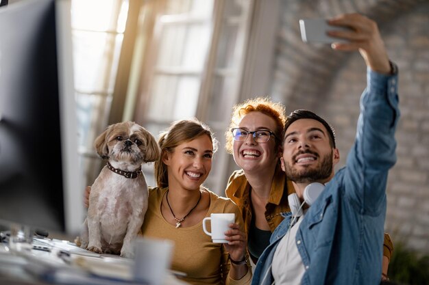 Team of young happy business people with a dog having fun while taking selfie in the office